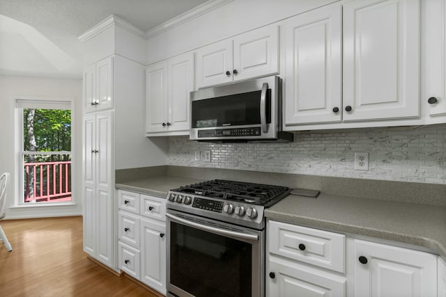 kitchen featuring white cabinets, tasteful backsplash, light wood-style floors, appliances with stainless steel finishes, and ornamental molding