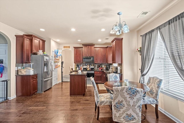 kitchen featuring a center island, dark wood-type flooring, backsplash, a chandelier, and appliances with stainless steel finishes