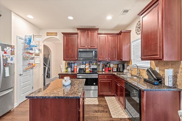 kitchen featuring hardwood / wood-style floors, backsplash, sink, appliances with stainless steel finishes, and a kitchen island