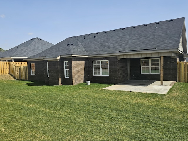 rear view of property featuring brick siding, a patio, a shingled roof, a lawn, and fence