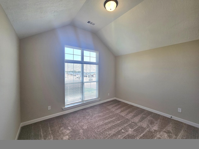 additional living space with vaulted ceiling, visible vents, dark carpet, and baseboards