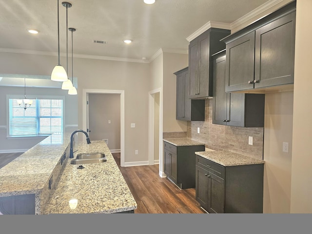 kitchen featuring light stone counters, visible vents, backsplash, a sink, and an island with sink