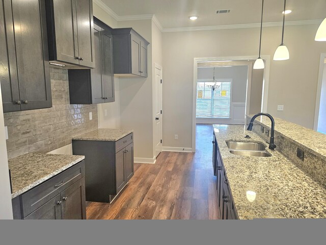 kitchen featuring light stone counters, dark wood finished floors, tasteful backsplash, ornamental molding, and a sink