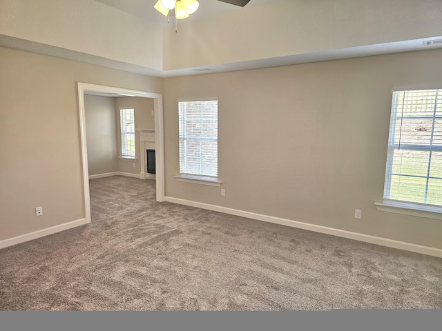 carpeted empty room featuring a glass covered fireplace, a healthy amount of sunlight, visible vents, and baseboards