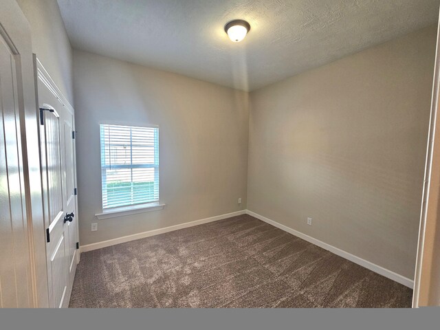 spare room featuring a textured ceiling, dark colored carpet, and baseboards