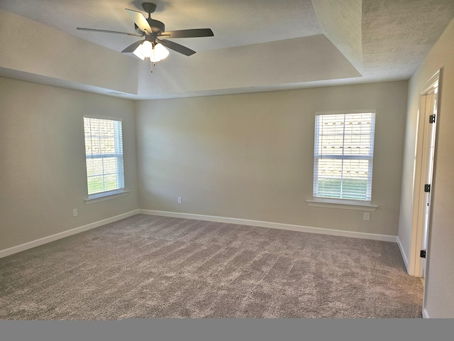 spare room with carpet floors, a tray ceiling, baseboards, and a ceiling fan