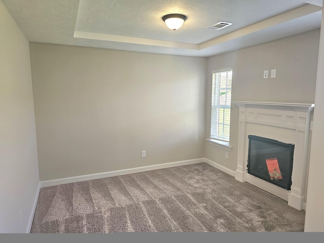 unfurnished living room featuring baseboards, a glass covered fireplace, a tray ceiling, a textured ceiling, and carpet flooring