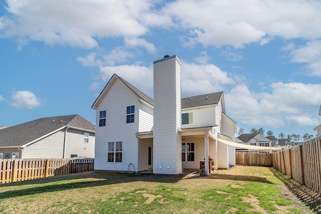 rear view of property featuring a lawn, a chimney, and a fenced backyard