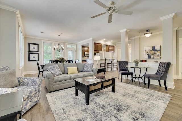 living room with ceiling fan with notable chandelier, decorative columns, ornamental molding, and light hardwood / wood-style flooring