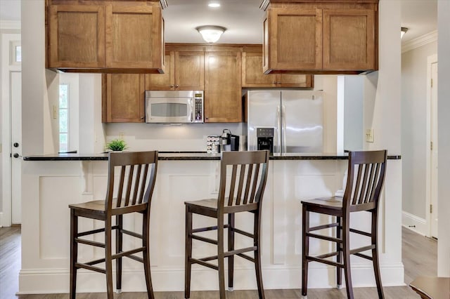 kitchen featuring a kitchen breakfast bar, dark stone countertops, ornamental molding, appliances with stainless steel finishes, and light hardwood / wood-style floors