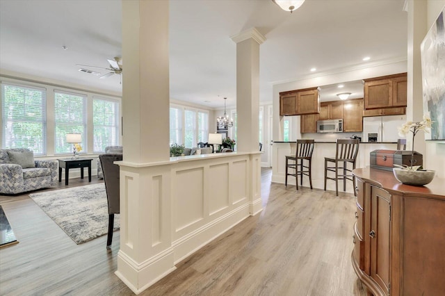 kitchen featuring ceiling fan with notable chandelier, crown molding, a kitchen bar, stainless steel appliances, and decorative columns