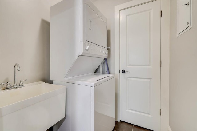 laundry room with dark tile patterned flooring, sink, and stacked washer and clothes dryer