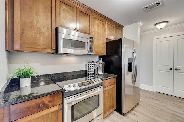 kitchen with dark stone countertops, crown molding, light hardwood / wood-style flooring, and stainless steel appliances