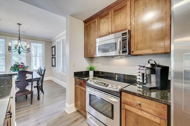 kitchen with an inviting chandelier, crown molding, pendant lighting, dark stone counters, and appliances with stainless steel finishes