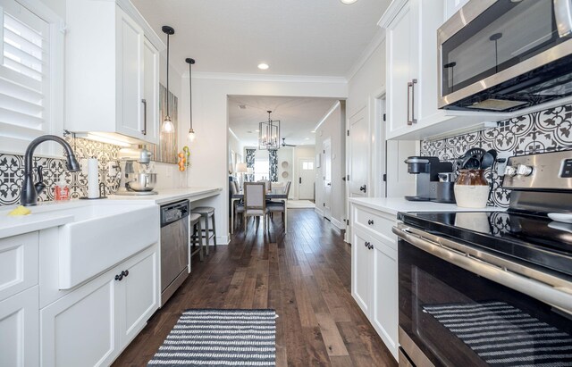 kitchen featuring white cabinetry, sink, stainless steel appliances, crown molding, and decorative light fixtures