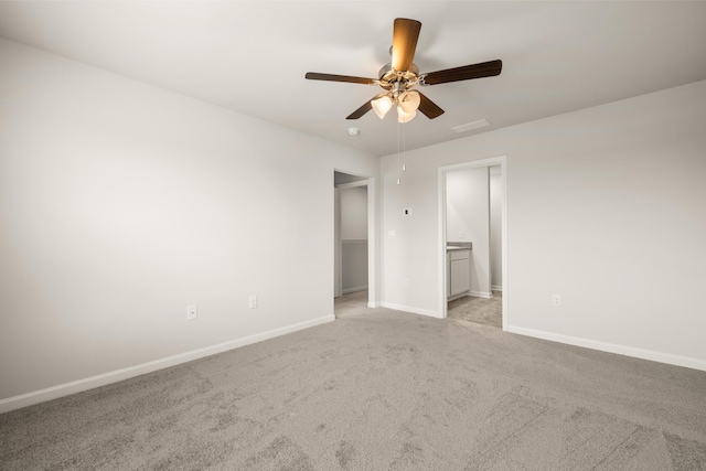 unfurnished bedroom with a walk in closet, light carpet, ceiling fan, and connected bathroom