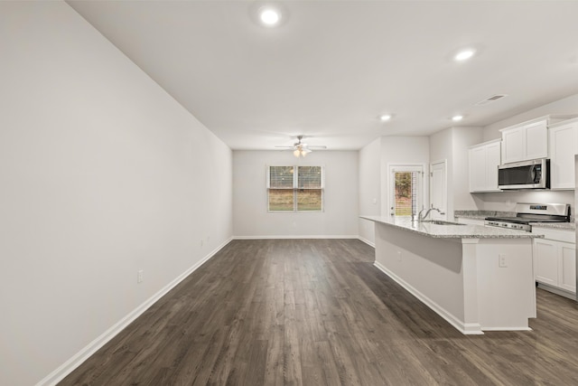 kitchen with stainless steel appliances, white cabinetry, a kitchen breakfast bar, light stone countertops, and a kitchen island with sink