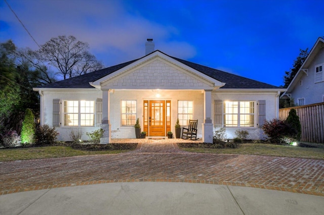 view of front of property with covered porch, brick siding, a chimney, and fence