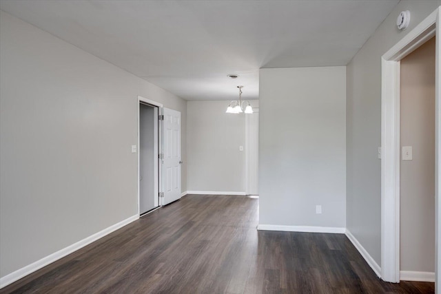 empty room with a notable chandelier, baseboards, and dark wood-style flooring