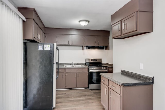 kitchen with light wood-type flooring, a sink, under cabinet range hood, dark countertops, and appliances with stainless steel finishes