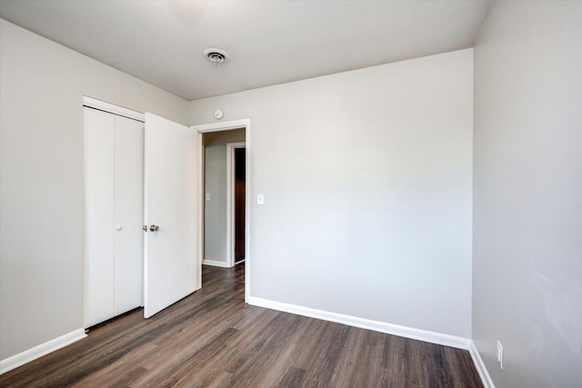 unfurnished bedroom with dark wood-type flooring, baseboards, visible vents, and a closet