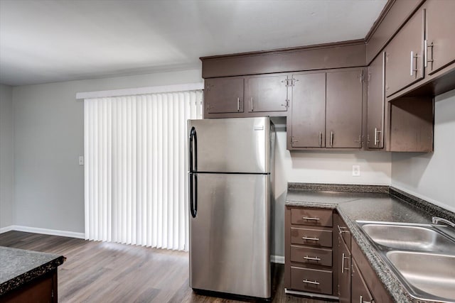 kitchen featuring dark countertops, a sink, dark brown cabinets, freestanding refrigerator, and dark wood-style flooring