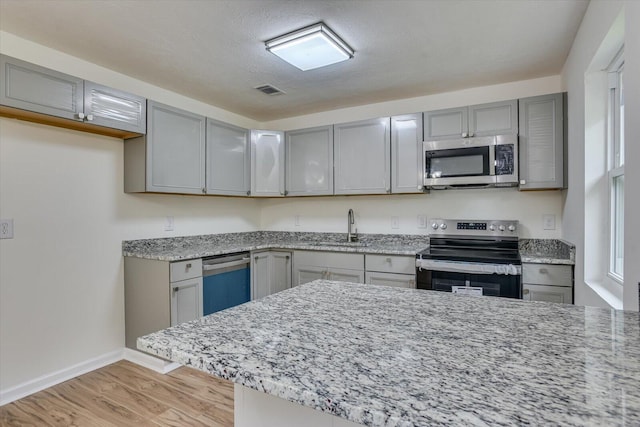 kitchen with gray cabinetry, sink, stainless steel appliances, and light hardwood / wood-style flooring