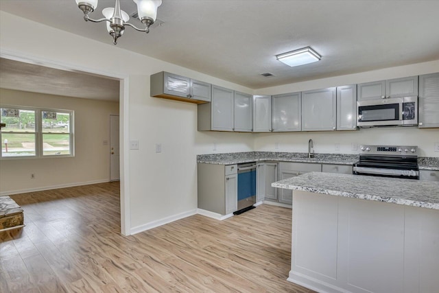 kitchen with gray cabinetry, sink, decorative light fixtures, appliances with stainless steel finishes, and light wood-type flooring