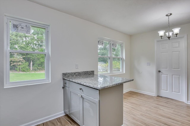 kitchen with an inviting chandelier, light stone counters, kitchen peninsula, decorative light fixtures, and light wood-type flooring