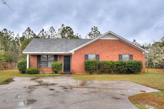 ranch-style house with brick siding, roof with shingles, a front lawn, and fence