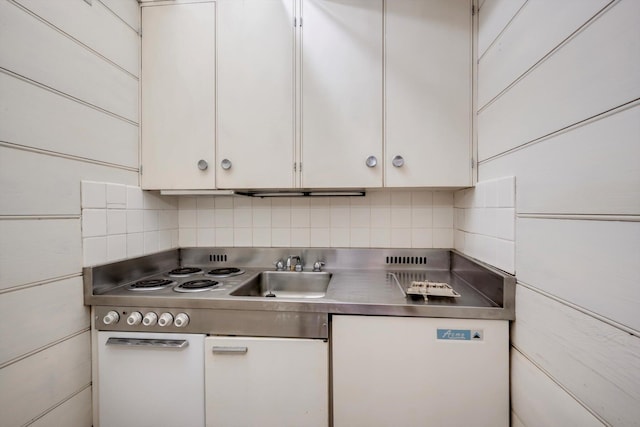 kitchen featuring stainless steel countertops, a sink, backsplash, and white cabinetry
