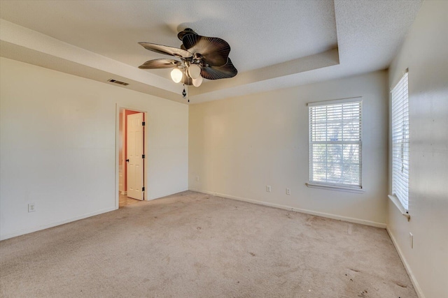 carpeted spare room with a textured ceiling, a ceiling fan, visible vents, baseboards, and a tray ceiling