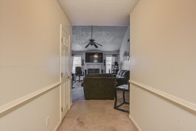 hall with a textured ceiling, baseboards, and light colored carpet