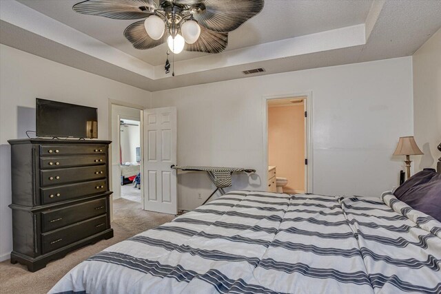 bedroom with carpet floors, a tray ceiling, visible vents, ceiling fan, and ensuite bath