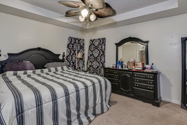 bedroom featuring light carpet, ceiling fan, a raised ceiling, and baseboards