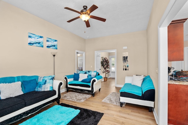 living room featuring ceiling fan, light hardwood / wood-style flooring, and a textured ceiling