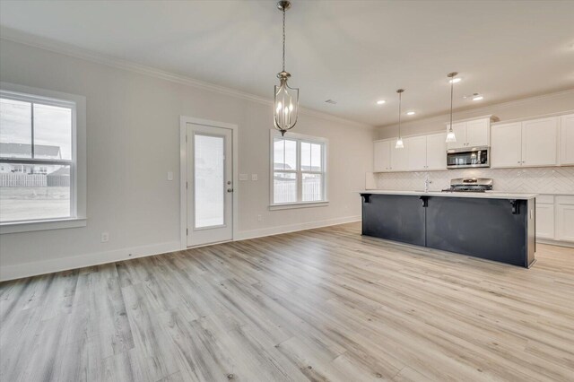 kitchen with white cabinets, stainless steel appliances, decorative light fixtures, and light hardwood / wood-style floors