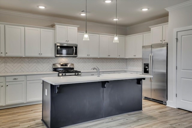 kitchen featuring appliances with stainless steel finishes, light wood-type flooring, a kitchen island with sink, decorative light fixtures, and white cabinetry