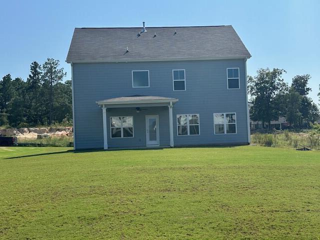 rear view of property with ceiling fan and a yard