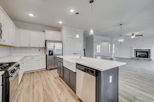 kitchen with stainless steel appliances, ceiling fan, decorative light fixtures, a center island with sink, and white cabinets