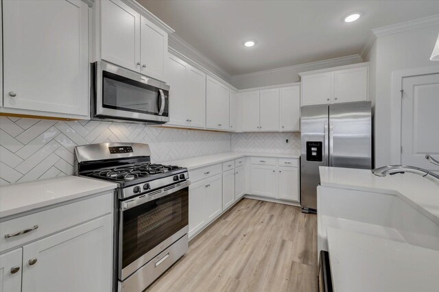 kitchen featuring appliances with stainless steel finishes, light wood-type flooring, tasteful backsplash, ornamental molding, and white cabinetry