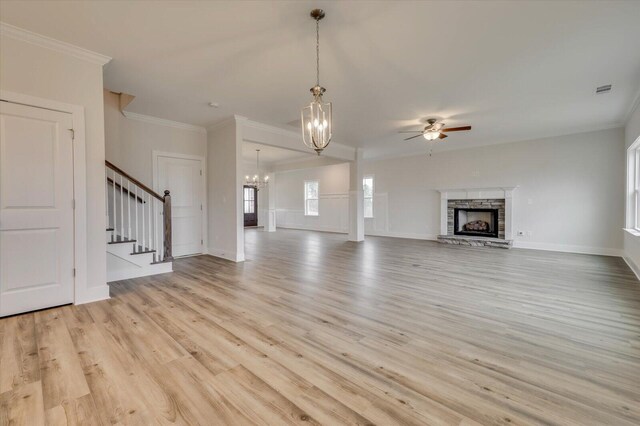 unfurnished living room featuring ornamental molding, ceiling fan with notable chandelier, light hardwood / wood-style flooring, and a stone fireplace