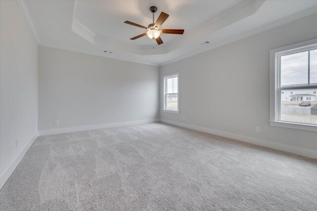 empty room with light colored carpet, ceiling fan, a raised ceiling, and ornamental molding