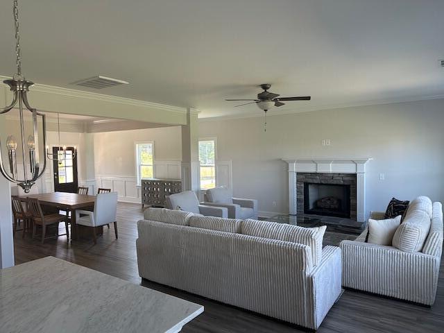 living room featuring ceiling fan with notable chandelier, dark wood-type flooring, a stone fireplace, and ornamental molding