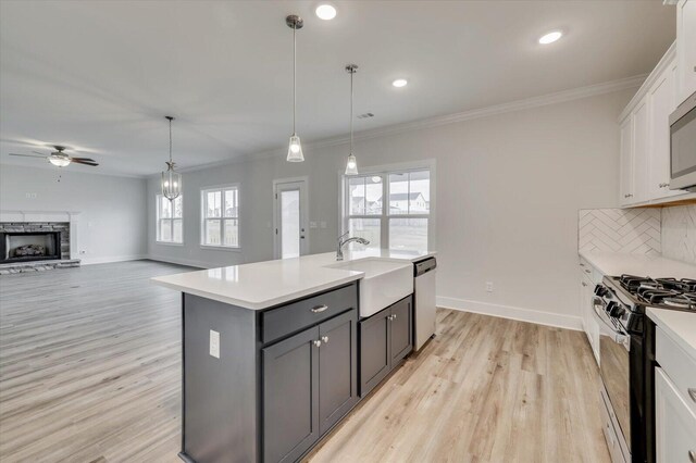 kitchen with stainless steel appliances, backsplash, a kitchen island with sink, white cabinets, and light wood-type flooring