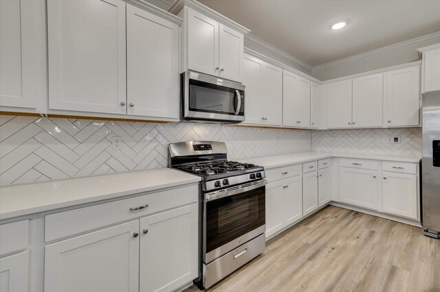 kitchen featuring white cabinets, crown molding, decorative backsplash, light wood-type flooring, and stainless steel appliances