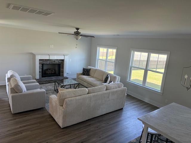 living room with ceiling fan, a stone fireplace, dark hardwood / wood-style floors, vaulted ceiling, and ornamental molding