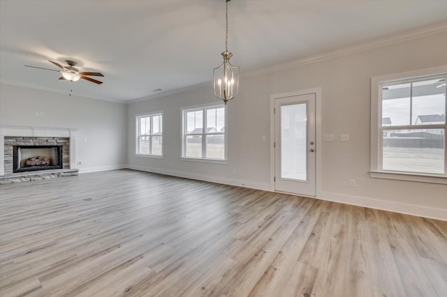 unfurnished living room featuring a stone fireplace, crown molding, light hardwood / wood-style flooring, and ceiling fan with notable chandelier