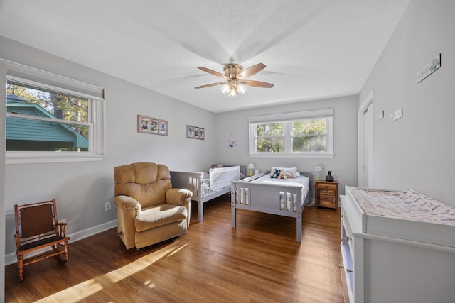 bedroom with ceiling fan, a crib, and dark wood-type flooring