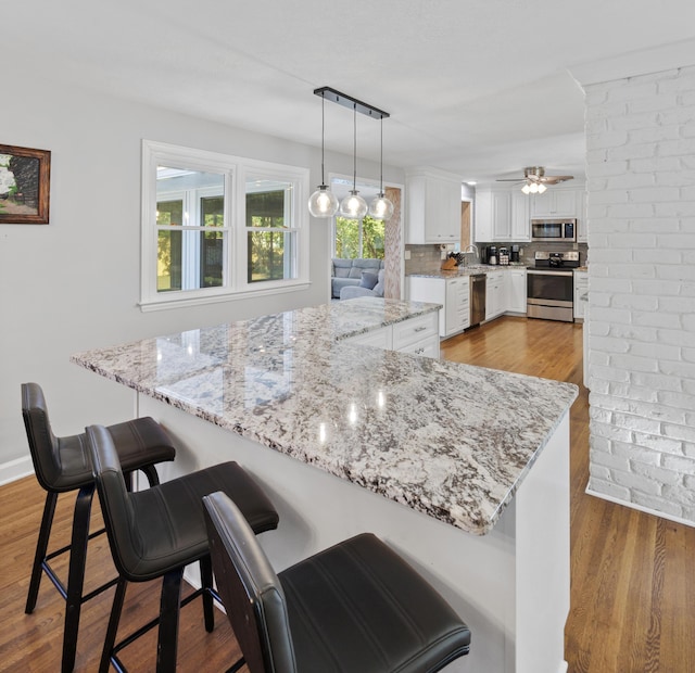 kitchen with white cabinets, decorative light fixtures, a kitchen bar, and stainless steel appliances